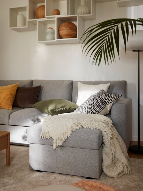 Es ist ein helles Wohnzimmer mit mehreren EKET Schränken an der Wand über einem BÅRSLÖV Bettsofa in Beige/Grau mit Bettwäsche zu sehen.