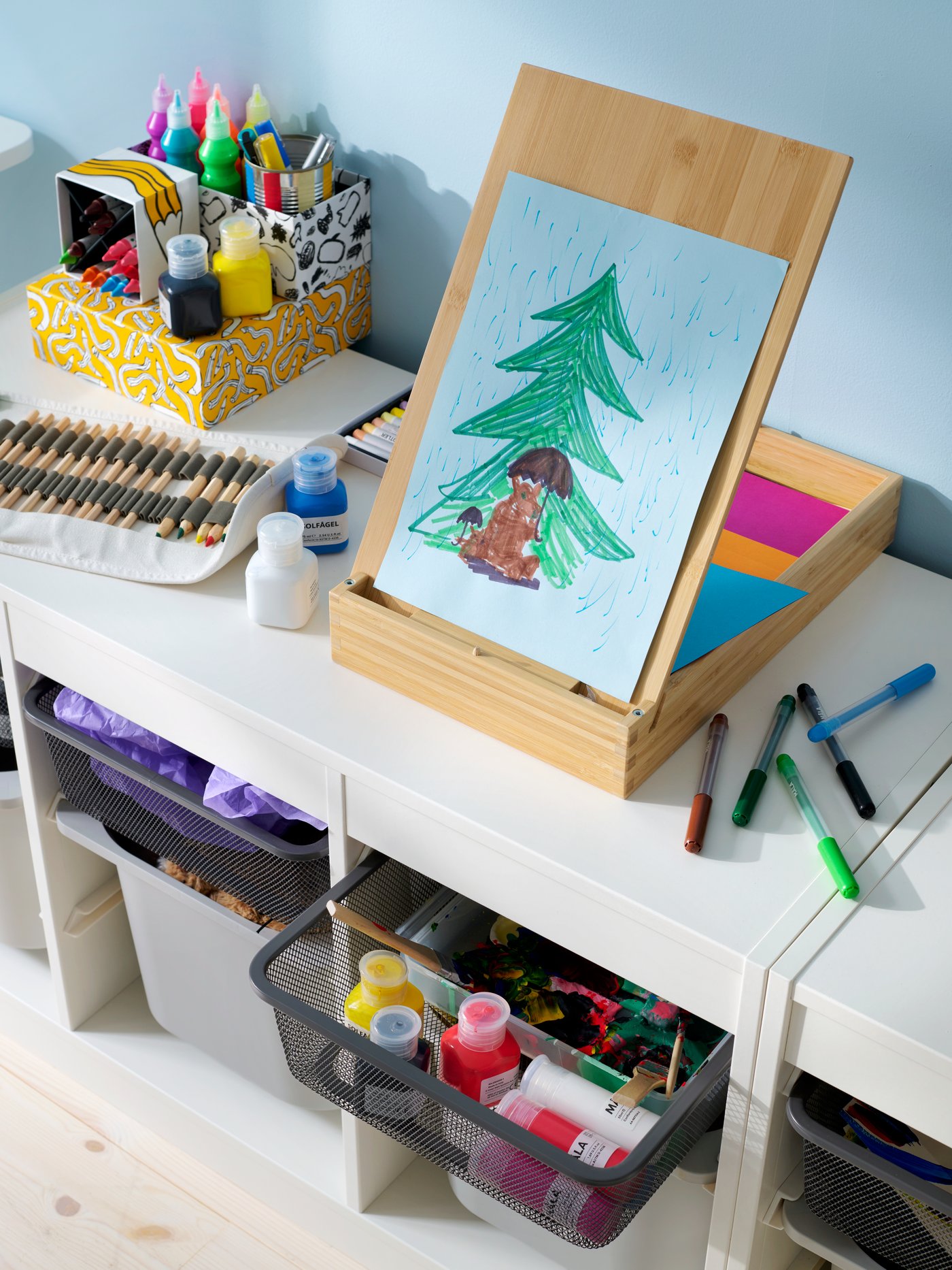 Close-up of a white TROFAST storage system with a mix of mesh and plastic boxes, SOLFÅGEL easel on top.