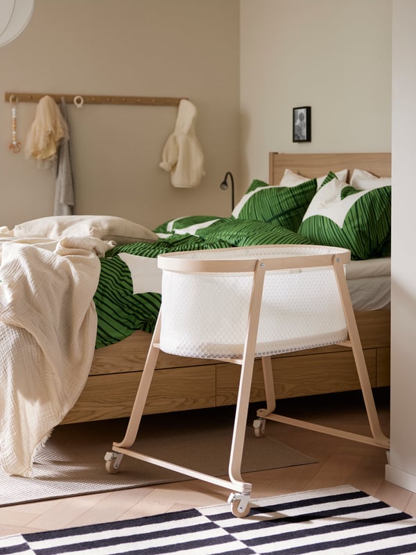ÄLSKVÄRD wieg met matras staat naast een TONSTAD bed met opbergruimte van eiken fineer opgemaakt met KUNGSCISSUS dekbedovertrekset.
