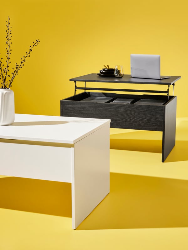 Two ÖSTAVALL adjustable coffee tables, one in white and one in black, are placed in a bright yellow space.