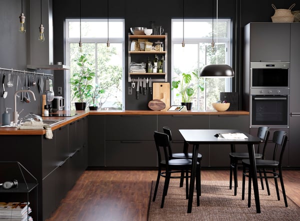 View of a large, L-shaped kitchen with dark cabinet fronts, a wooden worktop and a dining table with four dining chairs