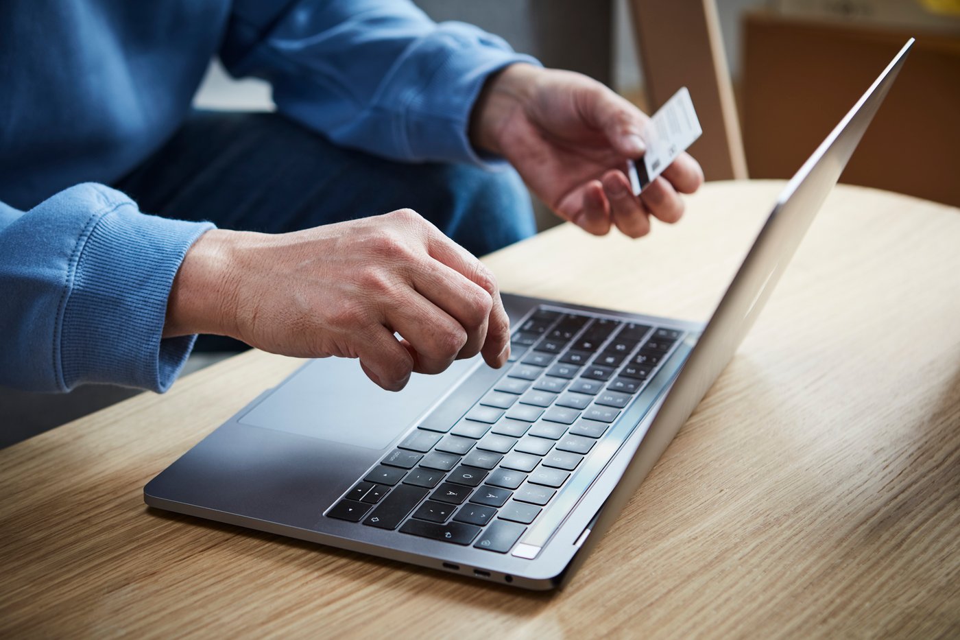 You see a laptop and a person's hands. There is a credit card in one hand.