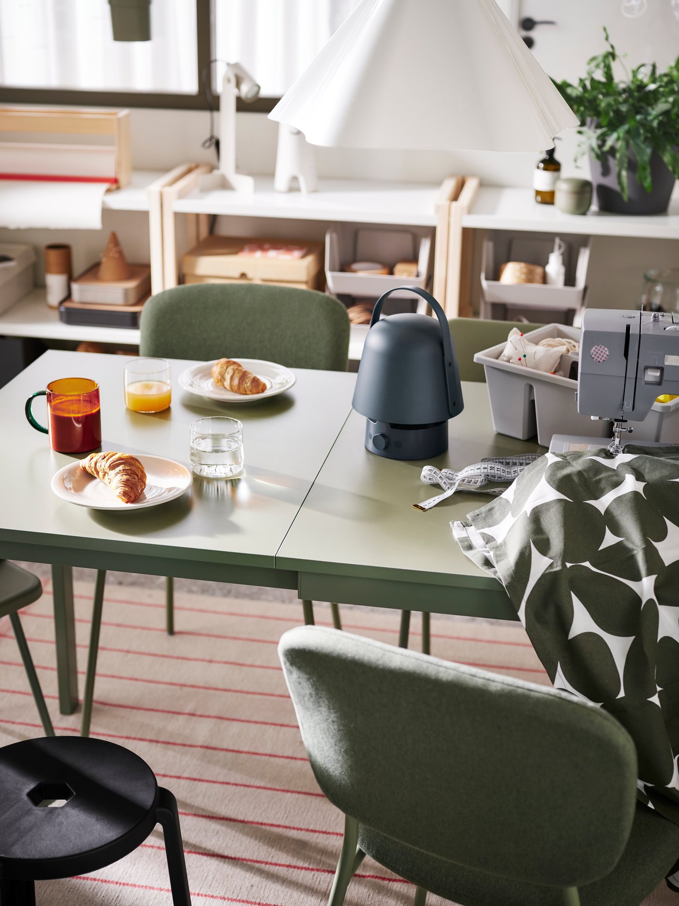 A VAPPEBY Bluetooth speaker lamp stands on a green VIHALS extendable table along with a SKUGGSTUBB mug and a sewing machine.
