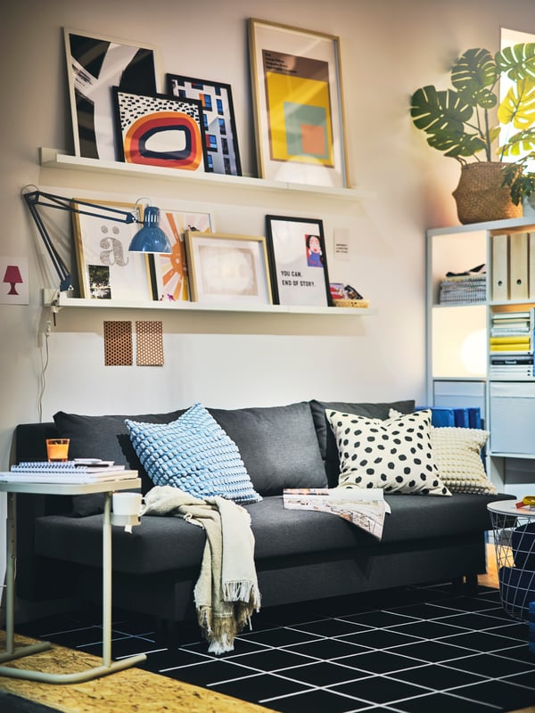 A dark grey ÄLVDALEN 3-seat sofa-bed on a black/white SVALLERUP rug, with a cushion in a pale blue SVARTPOPPEL cover on it.