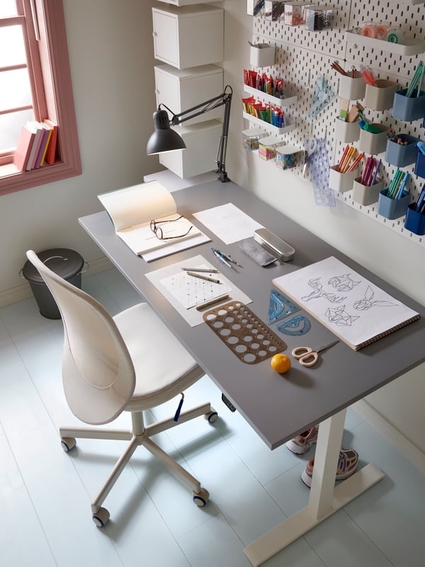 A neat and tidy workspace with a grey desk and white office chair and a pegboard with containers on the wall.