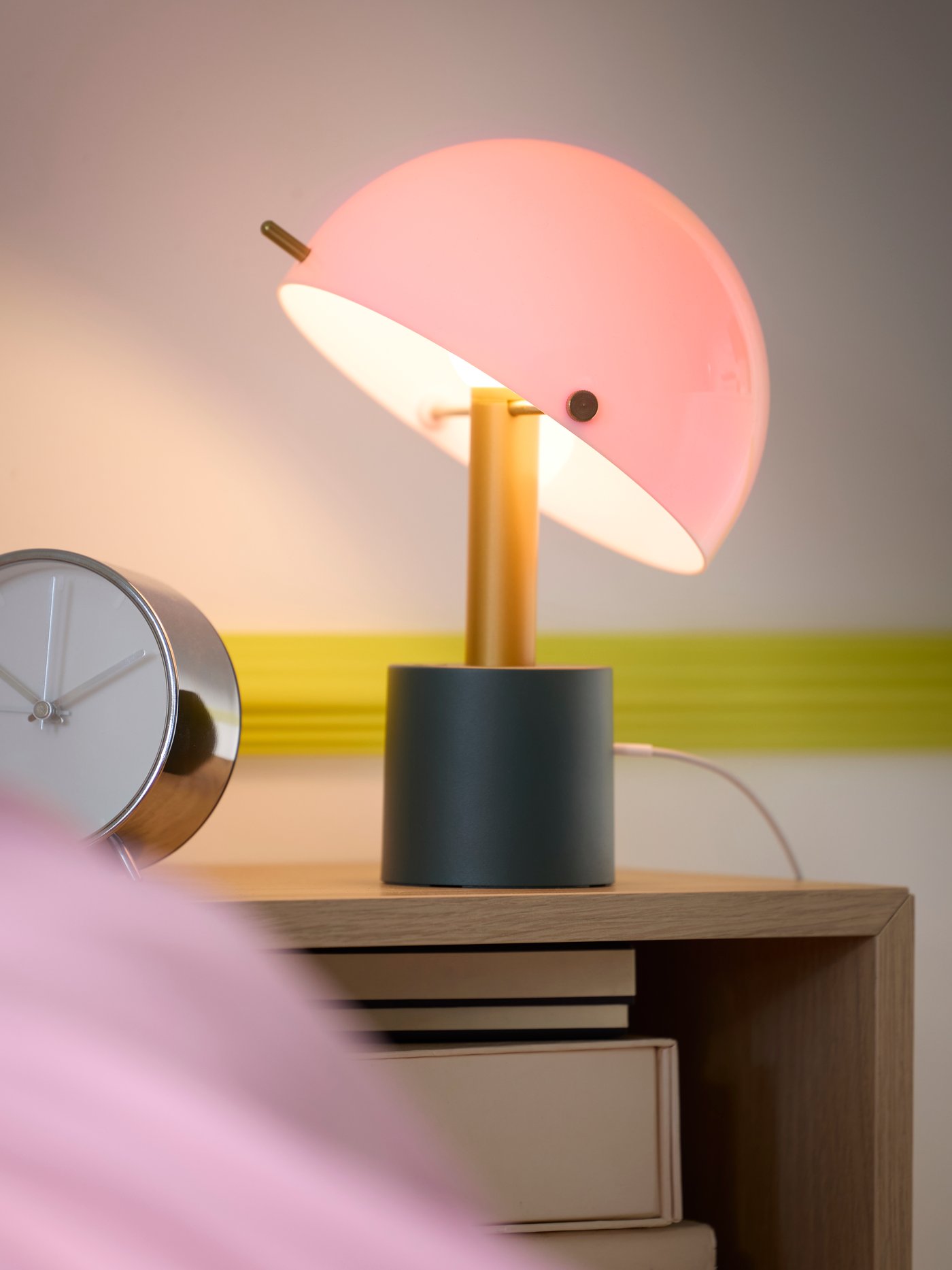 Närbild av NÖDMAST bärbar LED lampa i grönt och rosa, placerad på ett nattduksbord.

