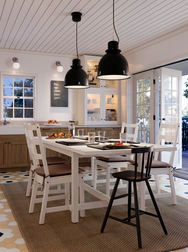 A white NORDVIKEN table with five chairs laid for a meal in the middle of a kitchen. Two SVARTNORA pendants hang overhead.