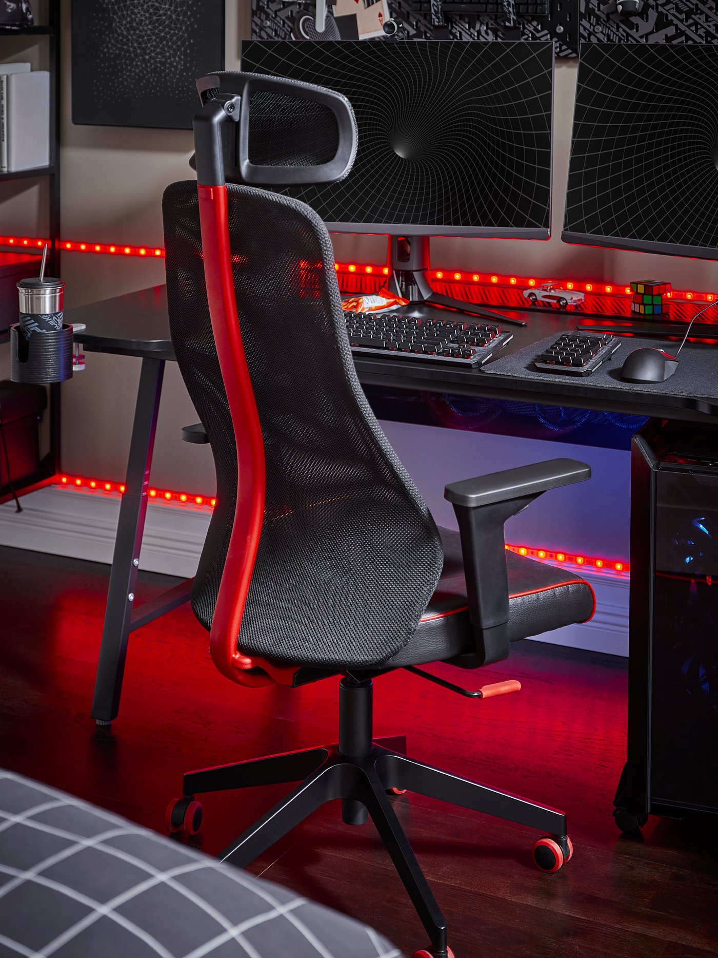 Un escritorio y silla gamer negro con rojo en un dormitorio oscuro iluminado con luces de neón.