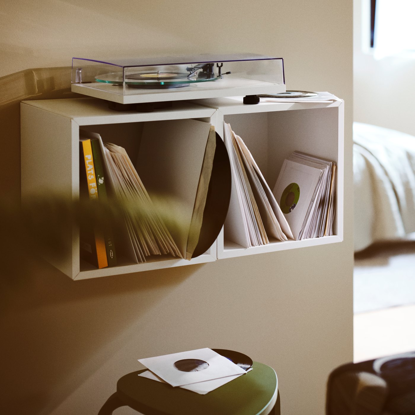 En vit, modern skivspelare står på en väggmonterad hylla fylld med en samling vinylskivor i ett rum med varm, omgivande belysning.