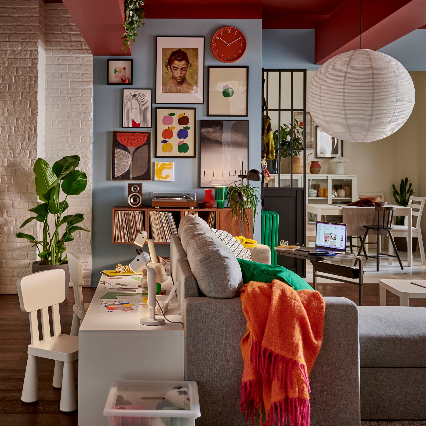 A living room with a vibrant wall featuring framed art, complemented by a green plant and a light-grey BLODFLÄDER picture.