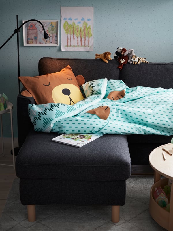 Un canapé 3 places doté d’une méridienne, un lampadaire/lampe de lecture à DEL noire, une housse de couette et taie ours turquoise, un livre.