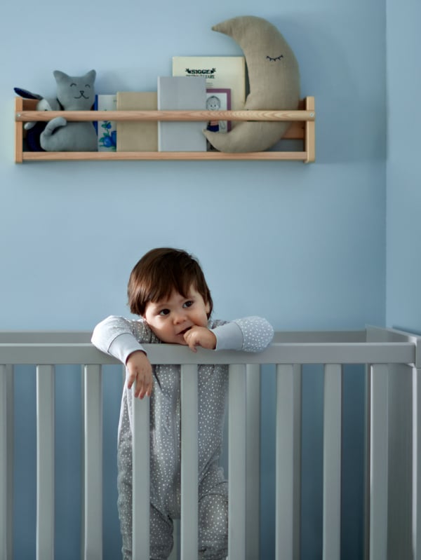 A SNIGLAR crib with mattress and a white LENAST fitted sheet by a brown wall, a cloud white UPPLYST LED wall lamp nearby.