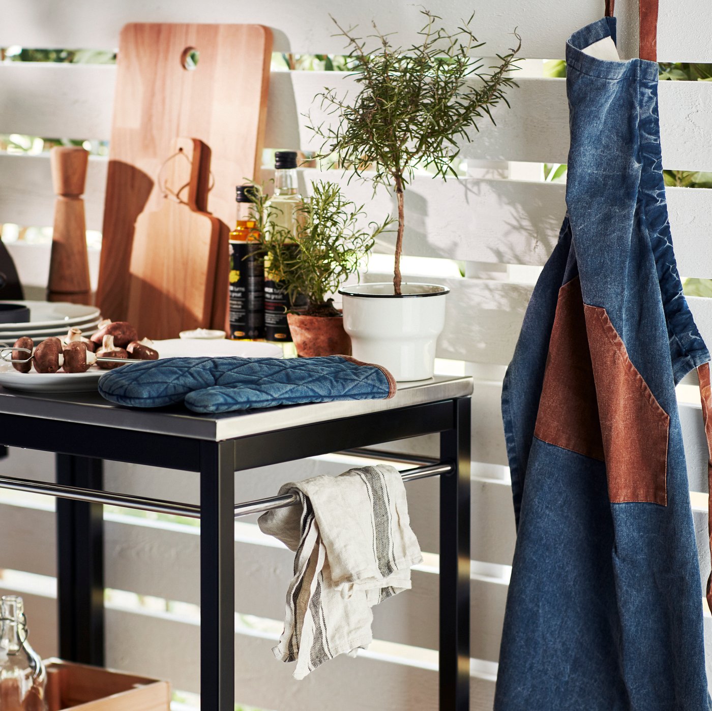 A KLASEN trolley in stainless steel with a GRILLTIDER oven glove in blue beside other items and a GRILLTIDER apron hanging.