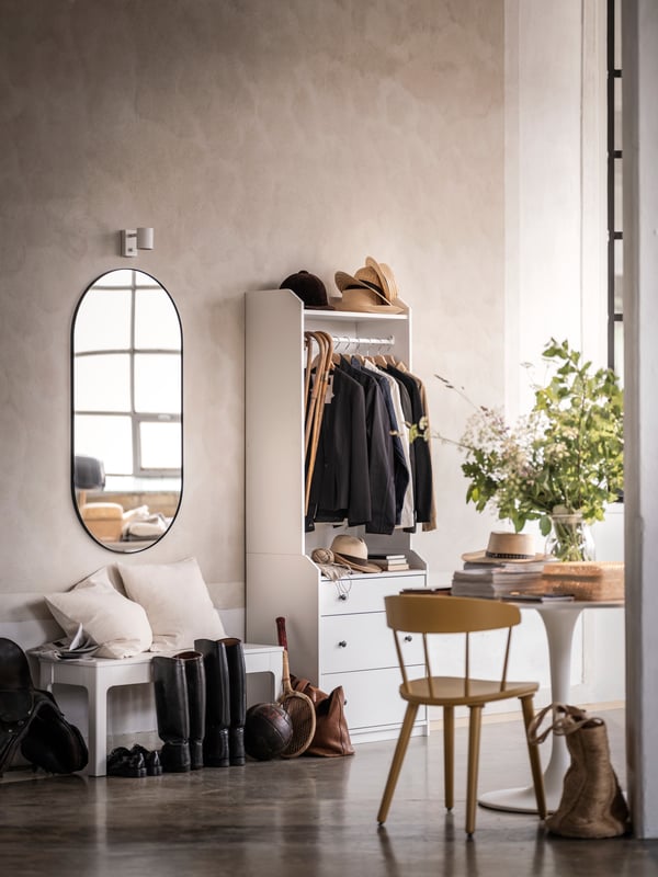 Une entrée avec des murs de couleur pierre dans laquelle des vestes sont suspendues à l'intérieur d'une armoire-penderie ouverte HAUGA. Un miroir ovale est accroché au mur.