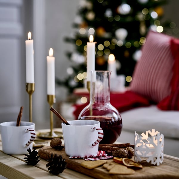 Sur une table décorée de façon festive, deux mugs et une carafe VINTERFINT contenant une boisson aux fruits épicée VINTERSAGA.