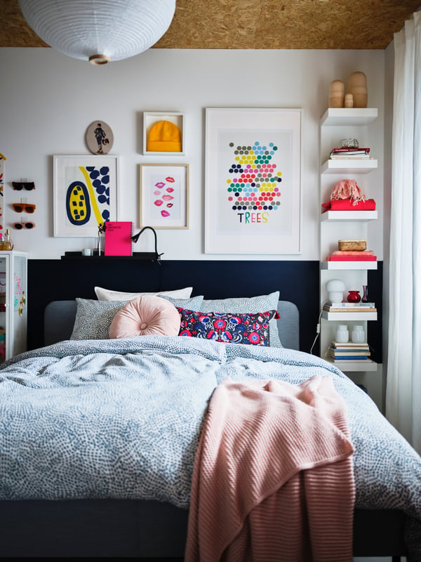 A bedroom with colorful decorations and a light-grey SLATTUM bed made with blue-and-white TRÄDKRASSULA bed linen.