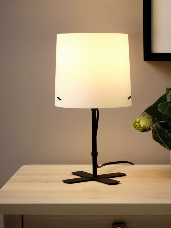 Una lámpara de mesa BARLAST encendida sobre una mesa de noche.