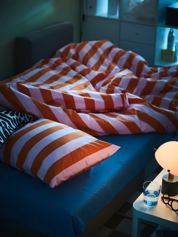 Zatamnjena soba u kojoj je ÄLVDALEN sofa ležaj namešten s MAJSMOTT posteljinom. NÖDMAST lampa je na obližnjem TINGBY pomoćnom stočiću.