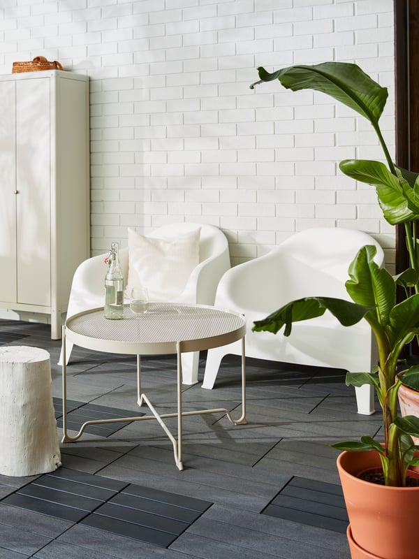 Two SKARPÖ outdoor armchairs and a KROKHOLMEN coffee table on a patio with RUNNEN floor decking in grey and black.