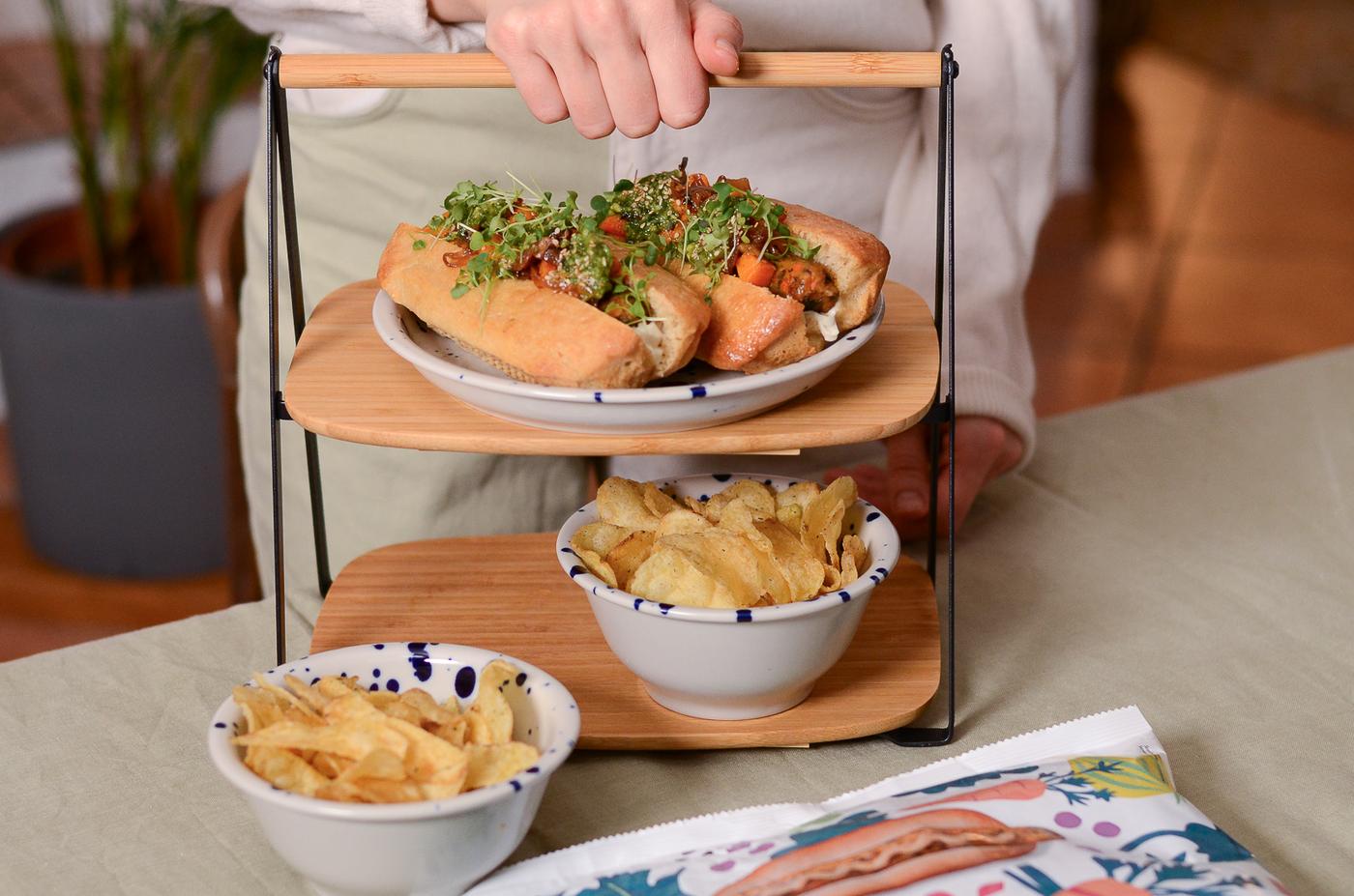 Eine Frau hält ein Tablett mit zwei Hotdogs und einer Beilage Pommes frites in der Hand, bereit, eine einfache Mahlzeit zu servieren.