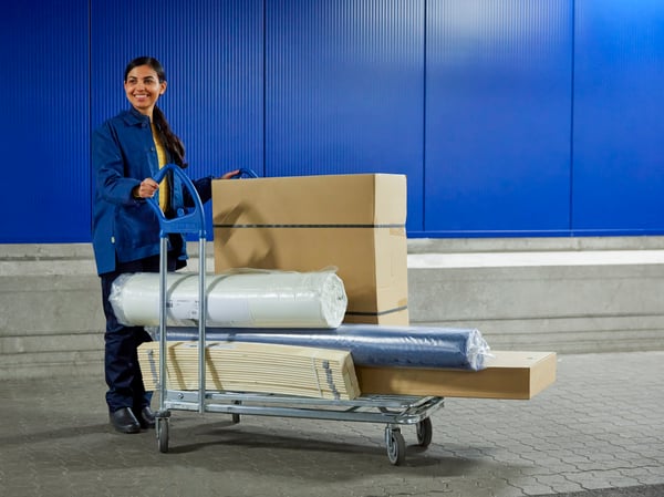 Zaposlena v podjetju IKEA z vozičkom, na katerem je naloženo blago.