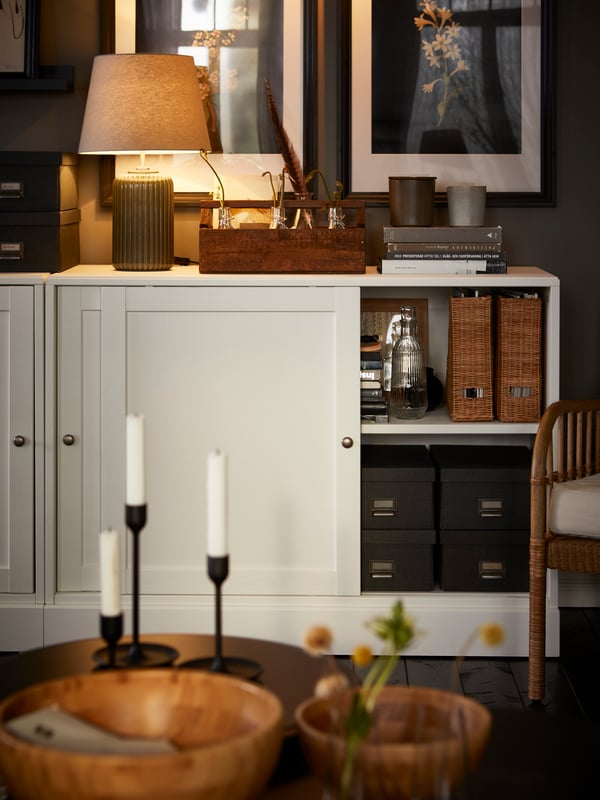 A white HAVSTA cabinet with plinth with a door slid open revealing neatly arranged boxes and magazines files.