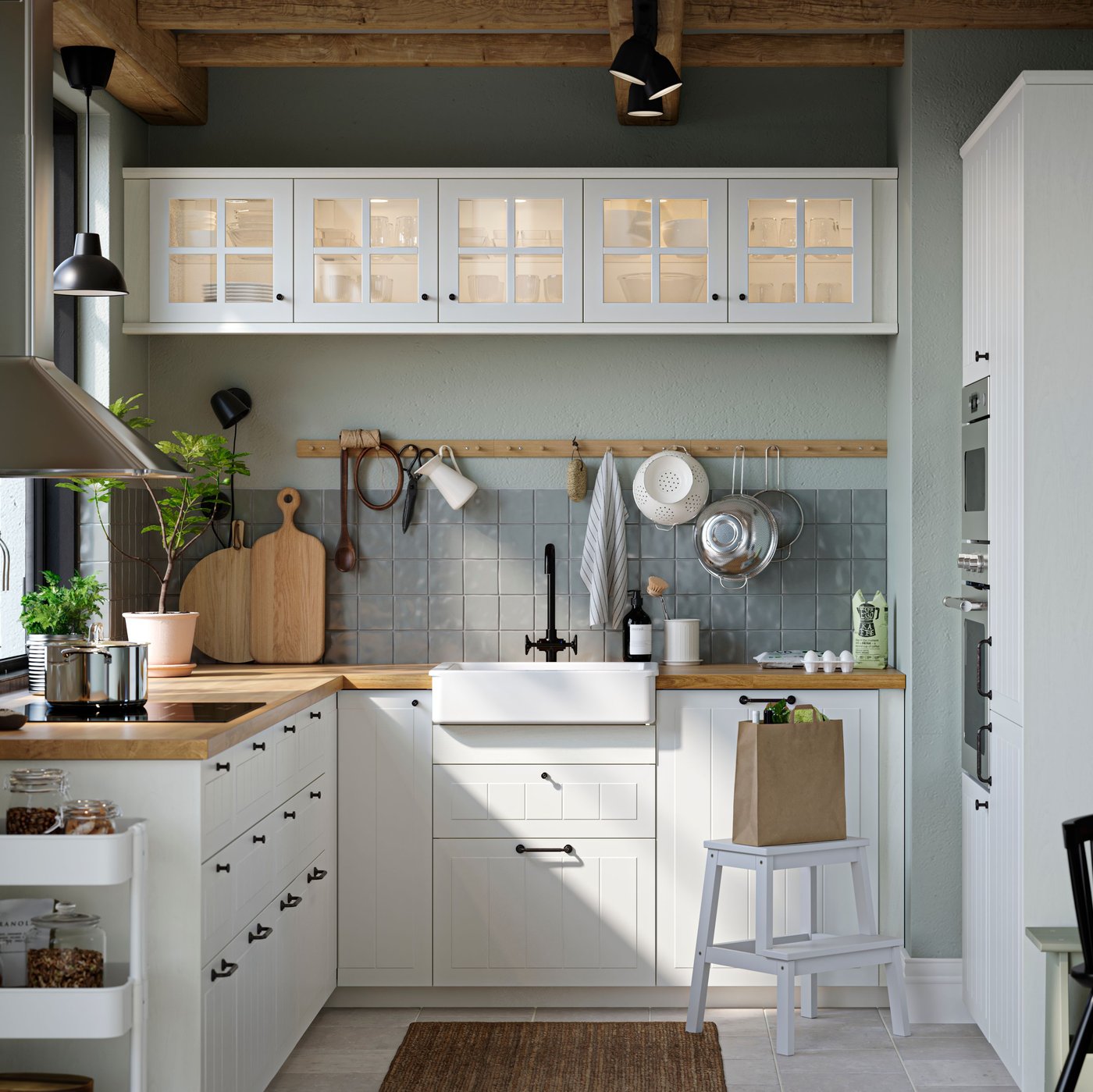 A kitchen with white STENSUND drawer fronts and glass doors, oak effect worktops and a white sink bowl with visible front.