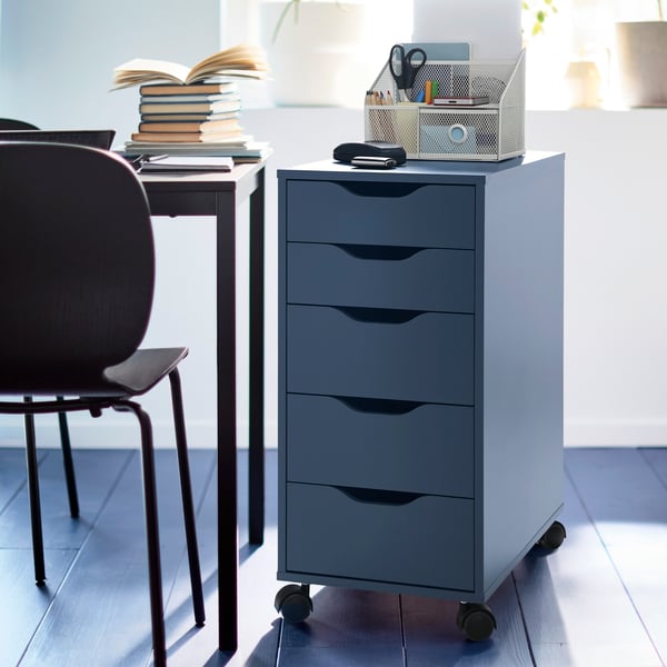 A black-blue ALEX drawer unit with five drawers on castors is positioned next to a desk and chair.