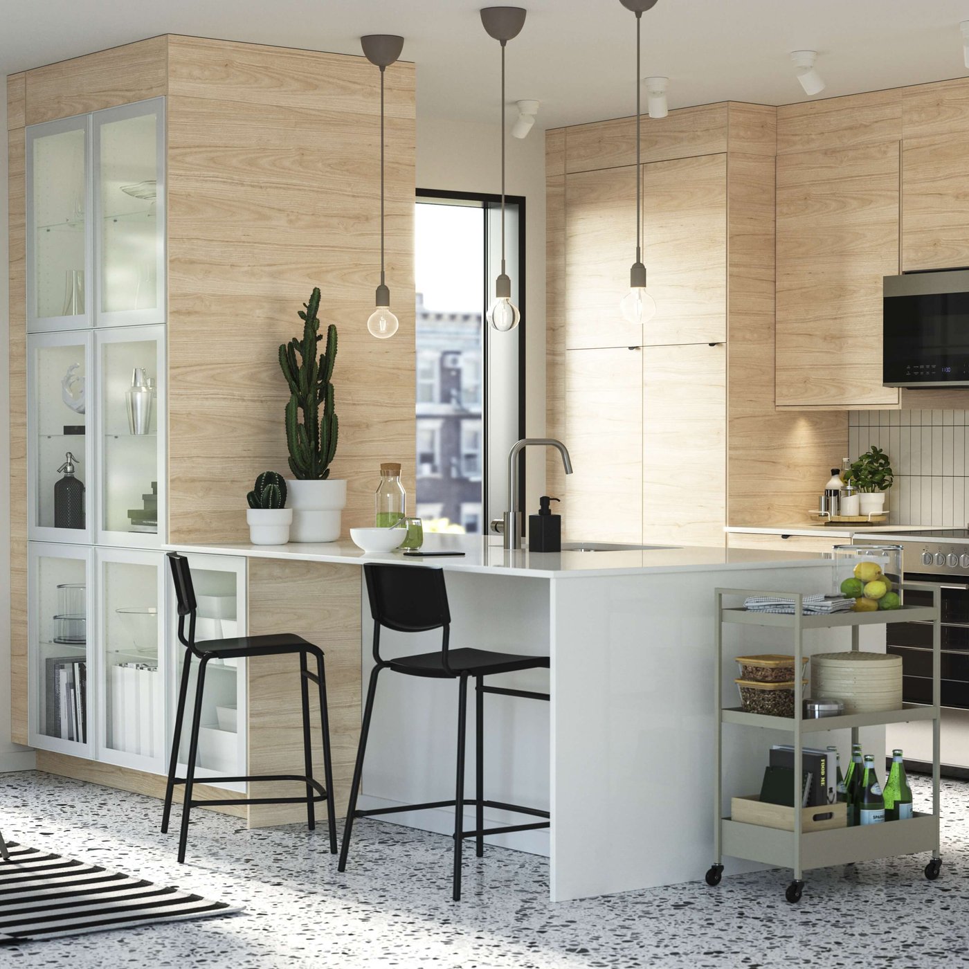 Modern kitchen with light wood cabinets, white island, black stools, pendant lights.