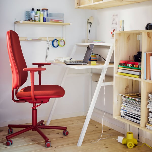 A red SMÖRKULL office chair with armrests stands at a white MITTPLAN desk in a corner of a room with white walls.