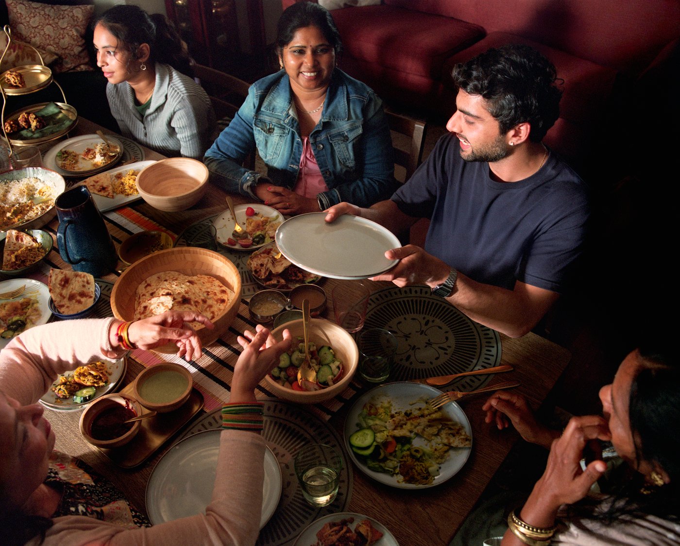 Un groupe de personnes souriantes est réuni autour d’une table, se passant des plats et des bols remplis de nourriture.