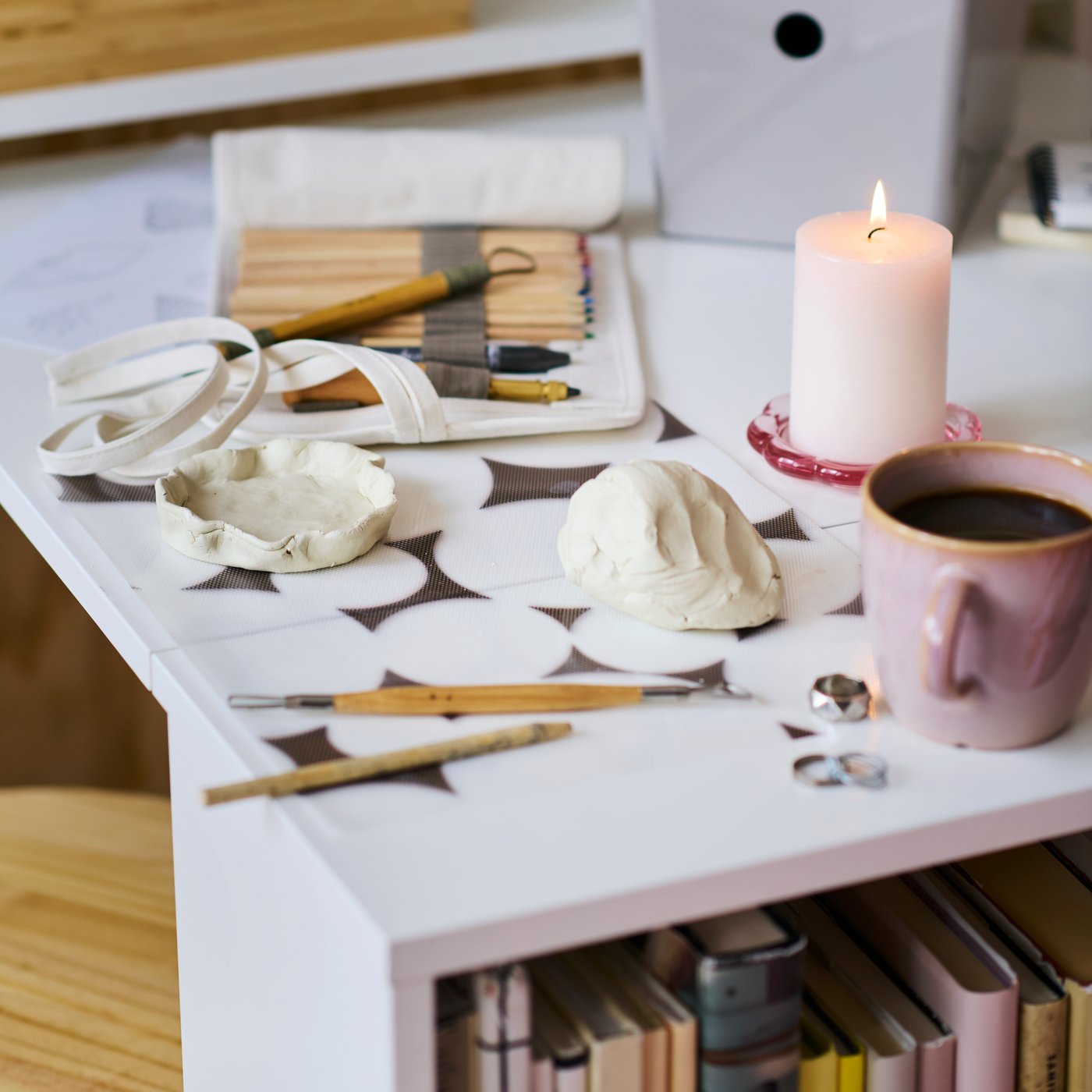 SOLFÅGEL pencil set in a roll-up pencil case and a pink cup on the fold-out table of a BILLY bookcase with foldable table.