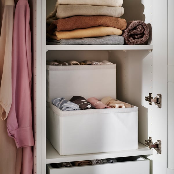 Two shelves in a PAX/TYSSEDAL wardrobe. One shelf holds SKUBB bins with clothes, and the other shelf holds sweaters.