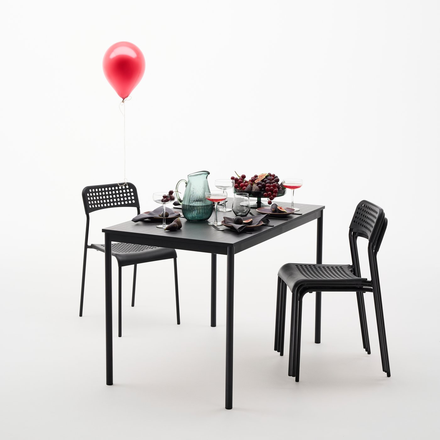 Une table à manger SANDSBERG noire est dressée pour quatre personnes avec de la vaisselle et des fruits. À côté de la table, il y a quatre chaises.