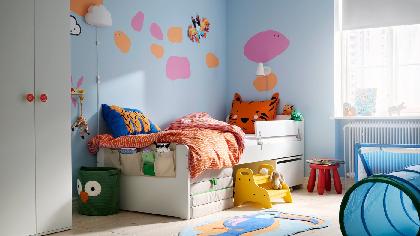 A children’s room with lots of colours, a SLÄKT bed along the light blue wall with pink and orange dots painted on it.