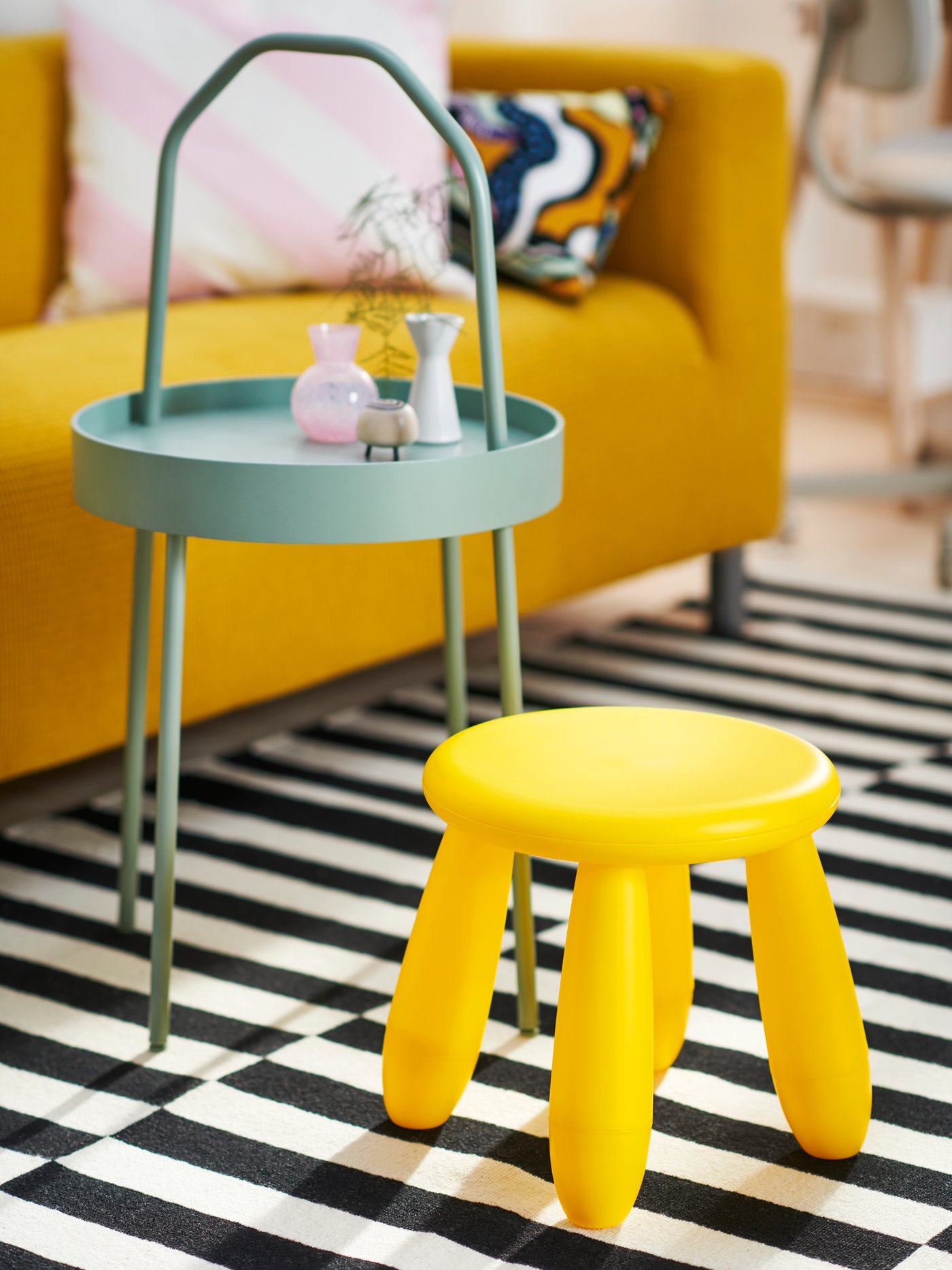A yellow MAMMUT children’s stool and a light grey-green BURVIK side table on top of a black/white stripe STOCKHOLM rug.