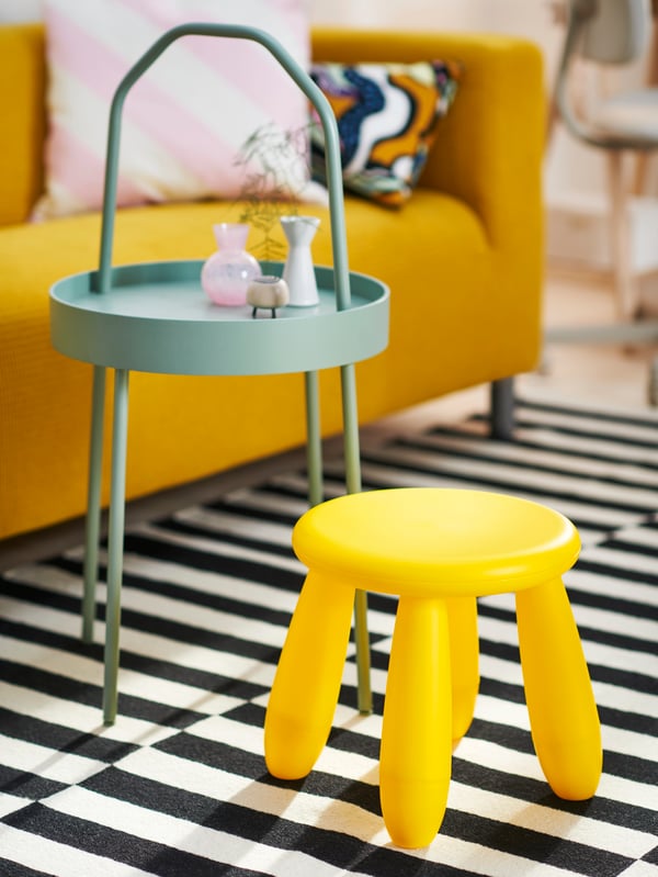 A yellow MAMMUT children’s stool and a light grey-green BURVIK side table on top of a black/white stripe STOCKHOLM rug.