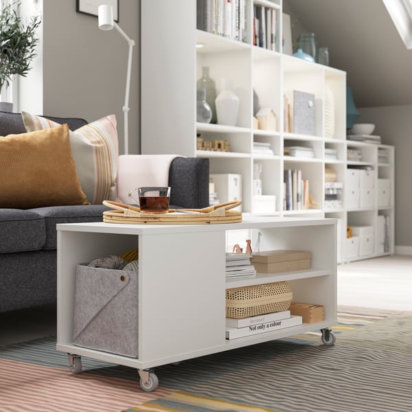 A white VIHALS coffee table with books and boxes on its shelves and a cup of tea on top stands in a living room.