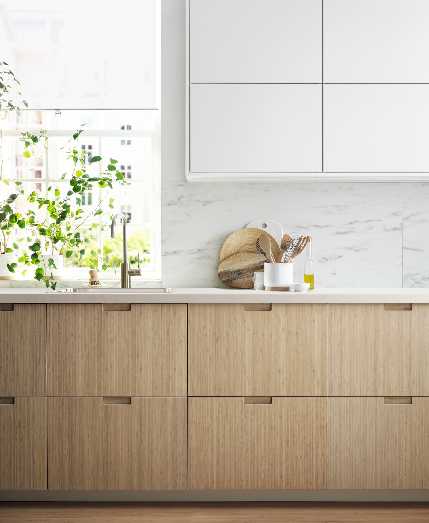 A kitchen with light bamboo FRÖJERED drawer fronts and white high cabinets.