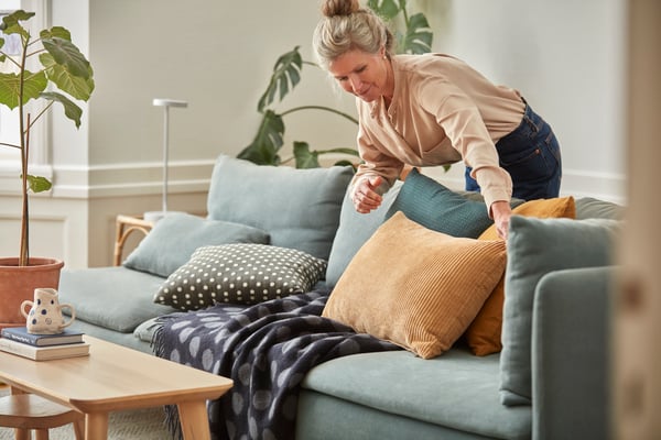 En kvinde retter på nogle puder i en sofa.