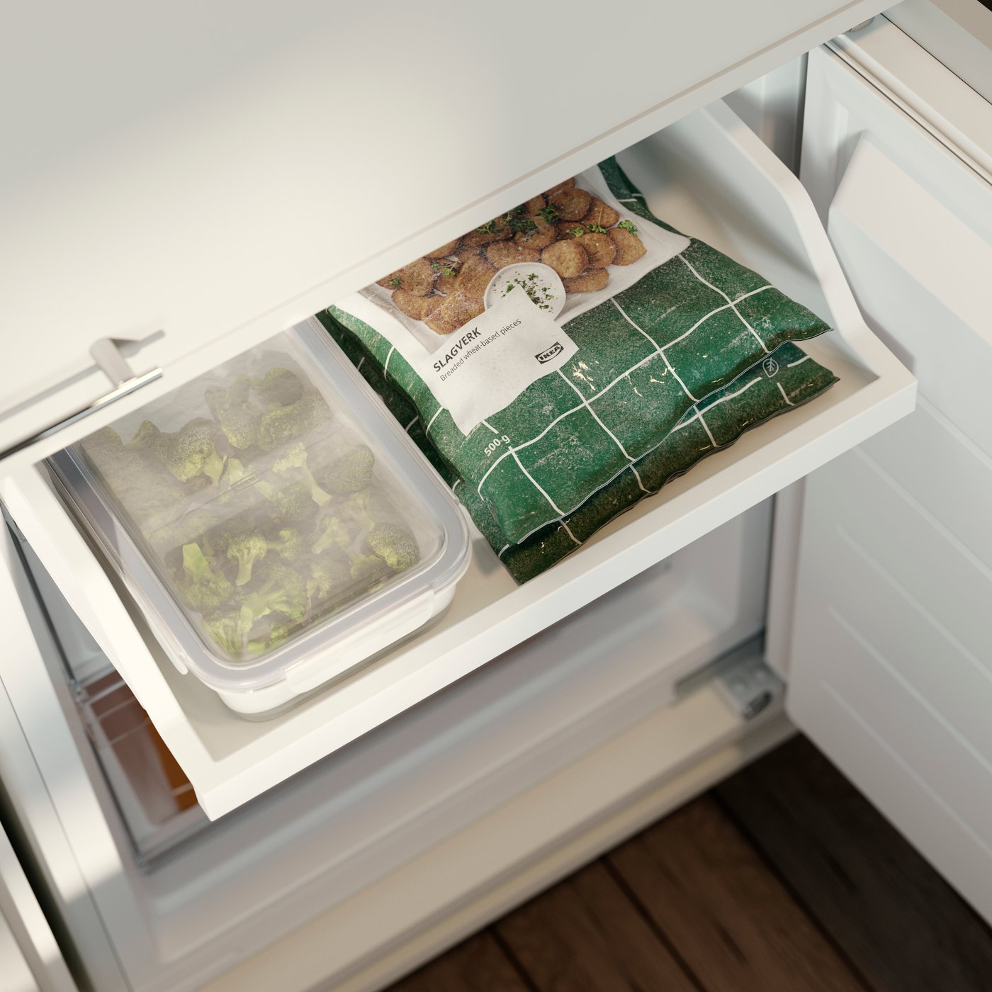 حافظة طعام IKEA 365+ بها خضراوات مخزنة في درج فريزر بجوار عبوات طعام مُجمد.  