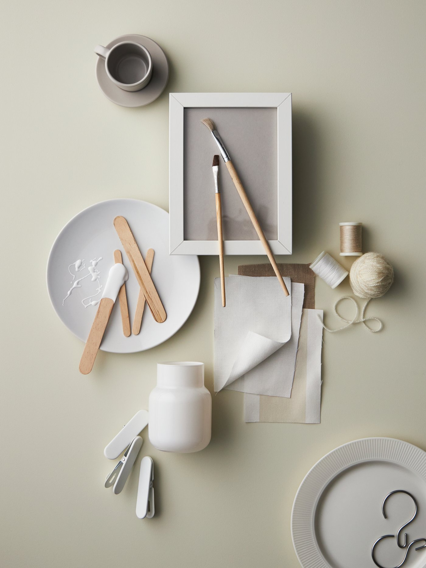 Des articles éparpillés, y compris une assiette à salade FLITIGHET blanche, une tasse à espresso DINERA beige avec sa soucoupe, du tissu et de la corde.