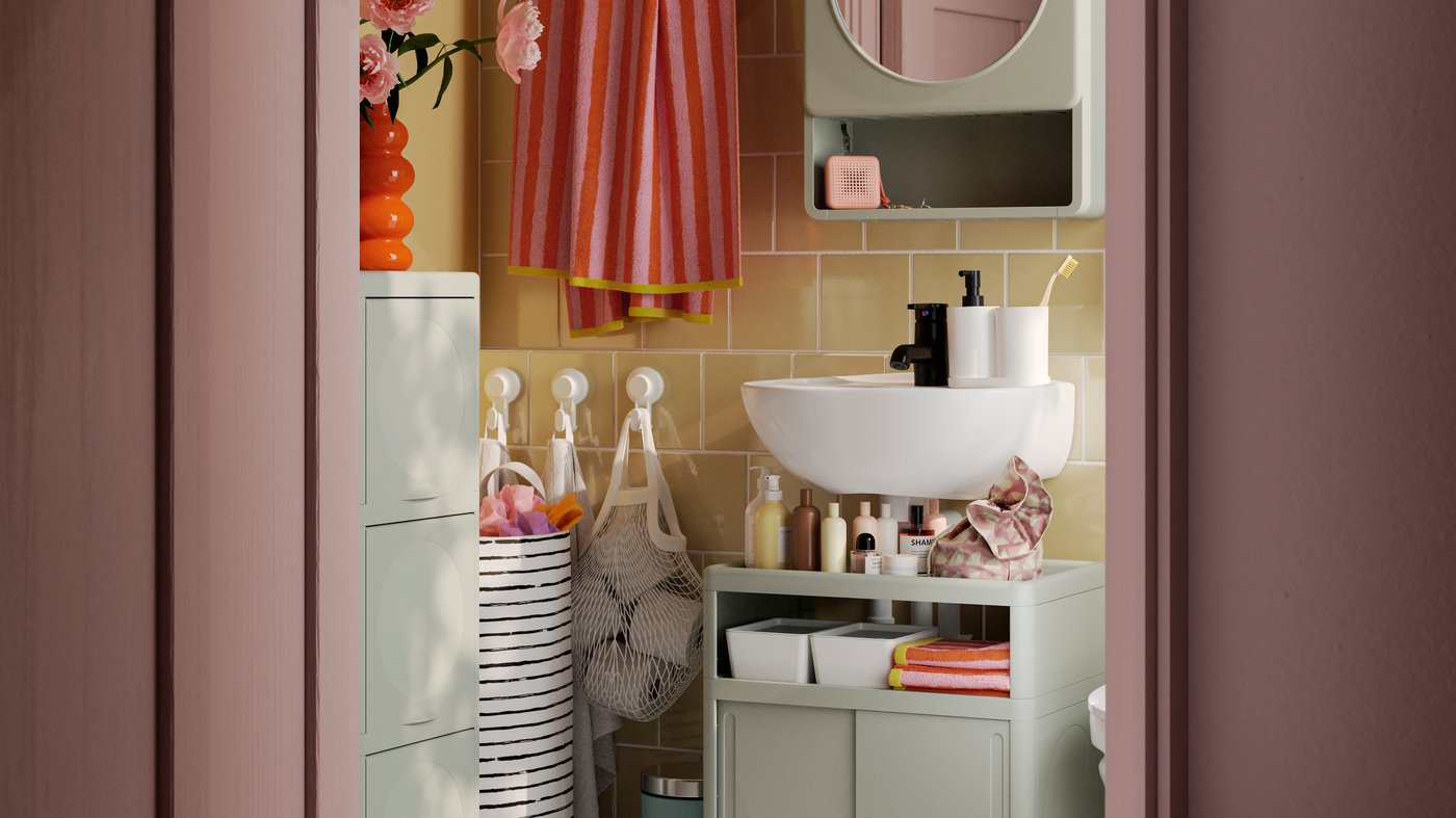 A green IVÖSJÖN wash-basin base cabinet, a cabinet with doors and a mirror cabinet are placed against a yellow-tiled wall.