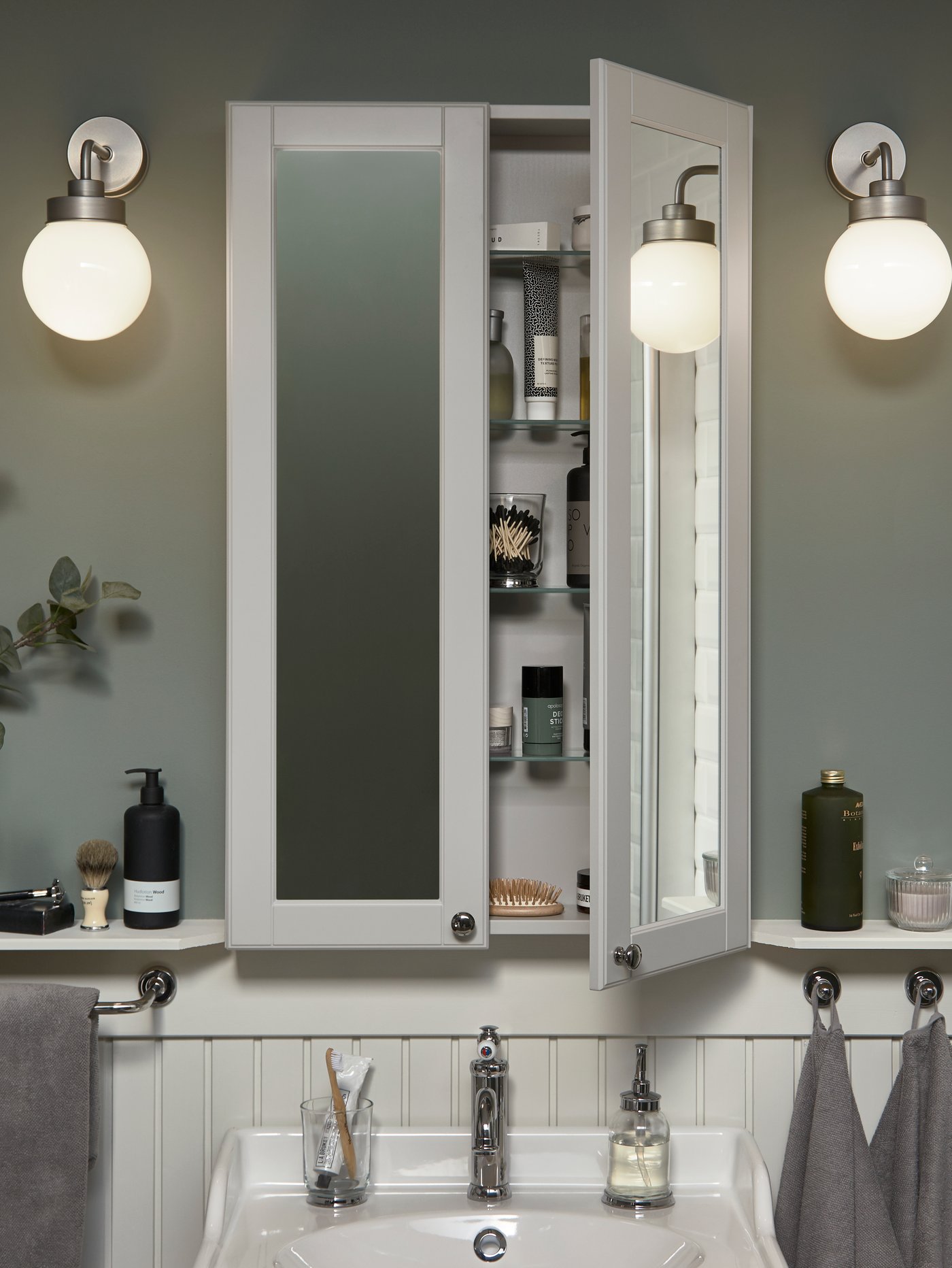 A shallow but high mirror cabinet over a white wash-basin. One door is open, and beauty items are stored inside.