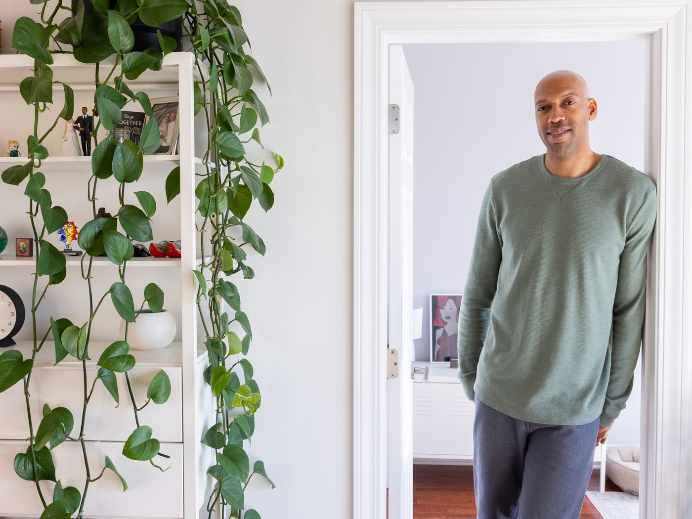 Man standing in clean white doorway, next to a bookcase with a plant hanging down.