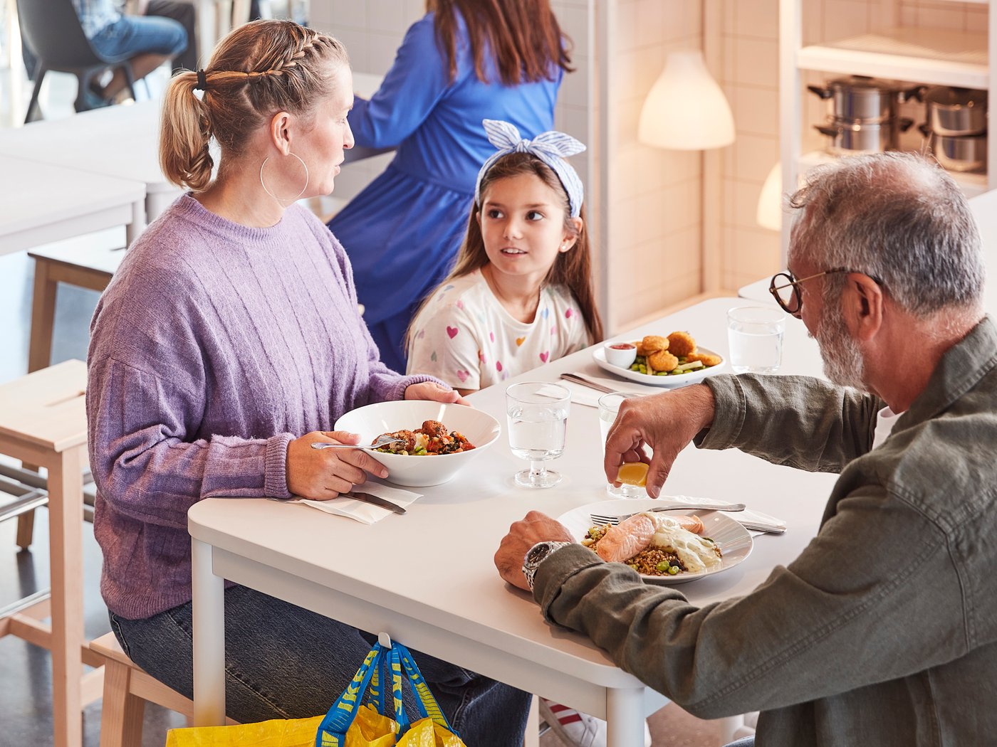 Dve odrasle osobe i dete uživaju u zajedničkom obroku za belim stolom u IKEA švedskom restoranu.