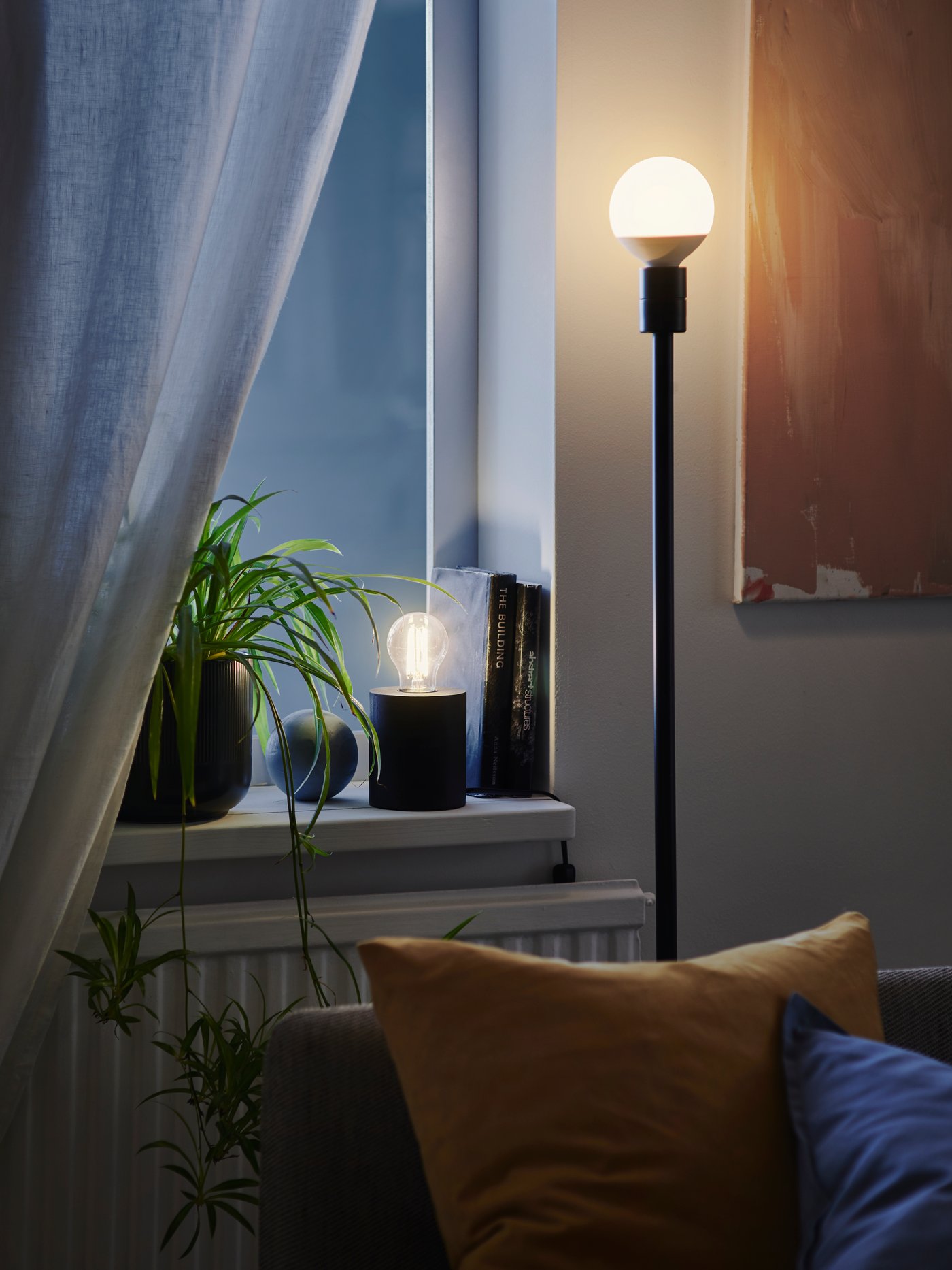 Un living con un sofá y detrás del sofá una lámpara de piso SKAFTET con una ampolleta LED SOLHETTA encendida.