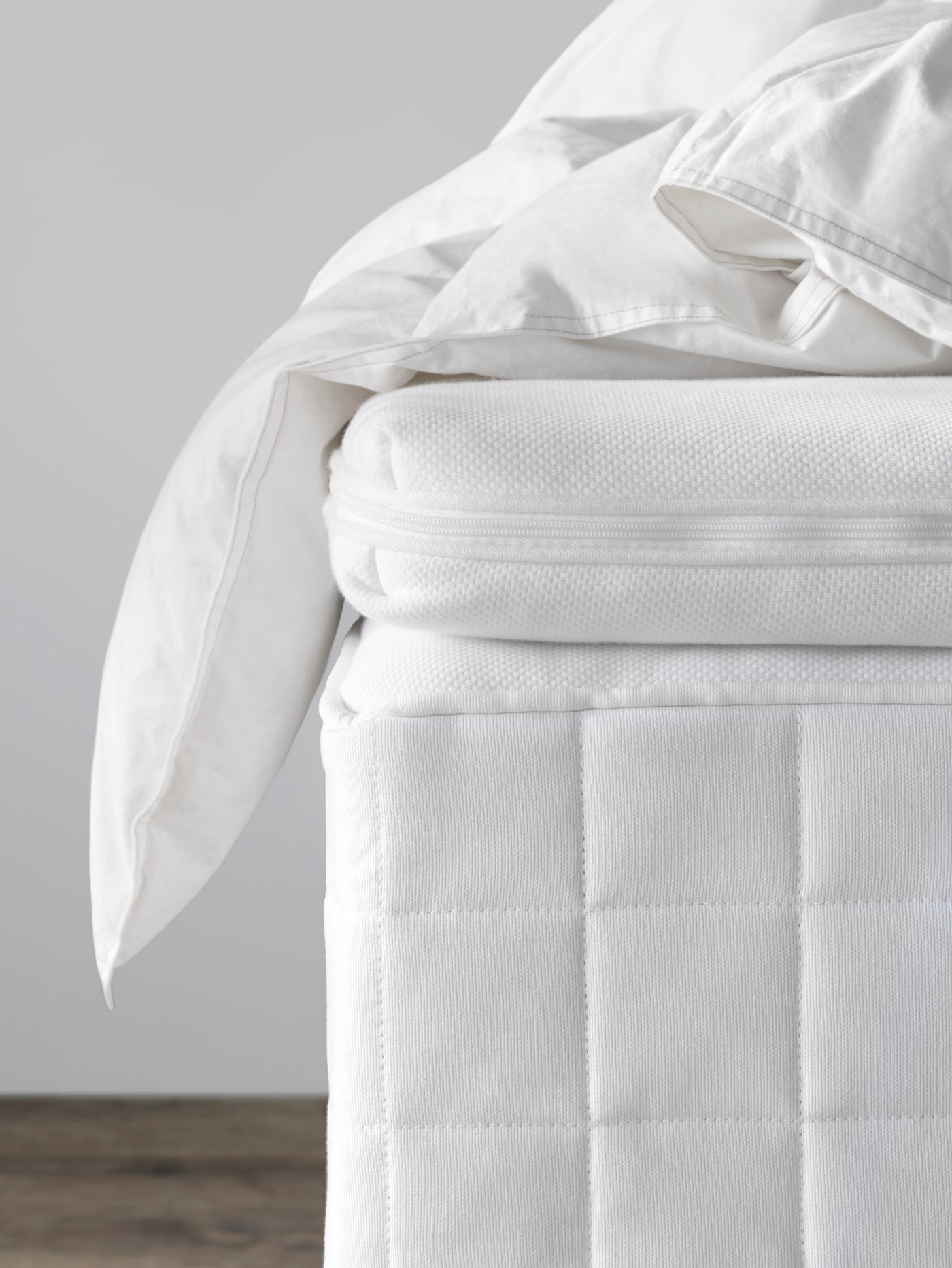 TUSSÖY mattress pad on top of the mattress with a duvet messily placed on top.