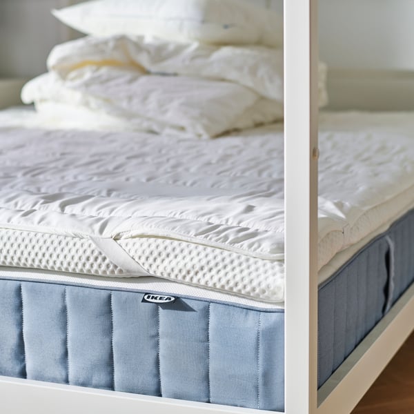 VITARNA four-poster bed with the different layers of mattresses visible, and a pile of duvets and pillows on top of it all.