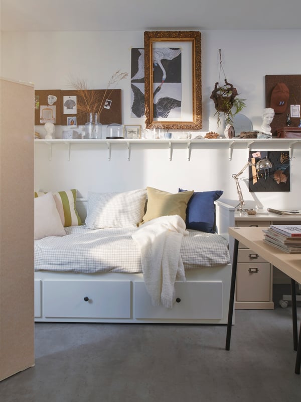 HEMNES 헴네스 데이베드에 HILDAMARIA 힐다마리아 쿠션이 세팅되어 있고 액자, 화초, 물건이 놓인 BURHULT 부르훌트 / SIBBHULT 십훌트 선반이 그 위에 있는 모습.